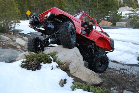 1989 Ford Bronco - A red off-road vehicle navigates a snowy, rocky terrain.