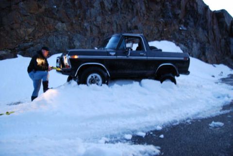 1989 Ford Bronco - A person attempts to free a classic Ford Bronco from a snowdrift on a rocky mountainside.
