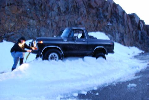 1989 Ford Bronco - A person attempts to free a black Ford Bronco from a snowdrift on a mountain road.