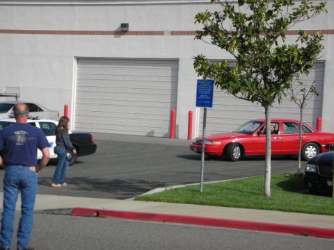 1998 Ford Crown Victoria - A red 1998 Ford Crown Victoria sedan is parked in front of a building with large garage doors.
