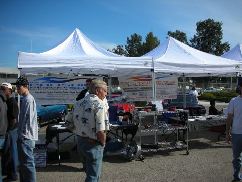 1998 Ford Crown Victoria - People gather at an outdoor car show, with tents displaying automotive parts and services.