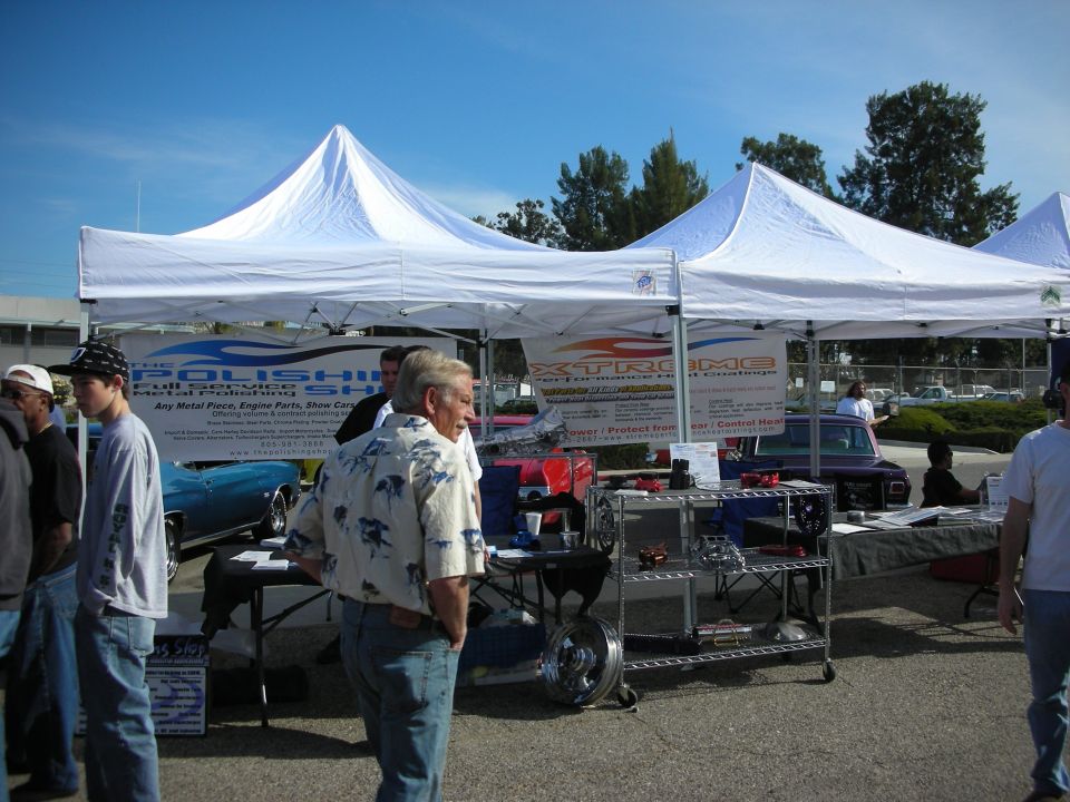 White vendor tents and a banner with people browsing at an outdoor car show