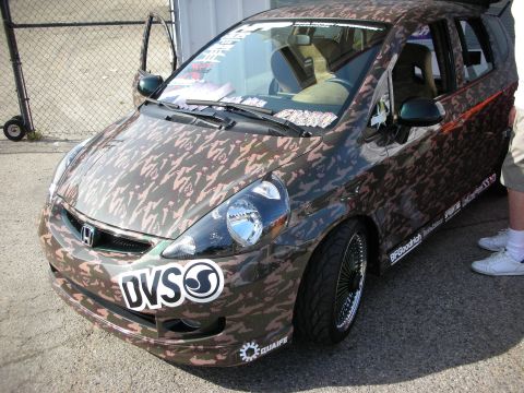 1998 Ford Crown Victoria - A customized Honda Fit with a camouflage wrap and aftermarket wheels is parked outdoors.