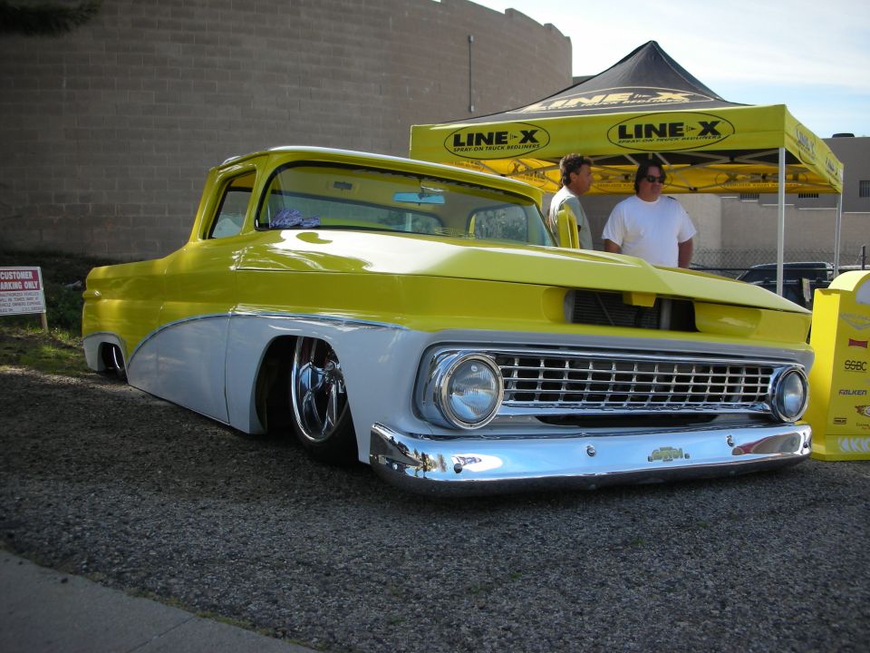 Lowered yellow-and-white custom classic Chevy pickup by a Line-X tent