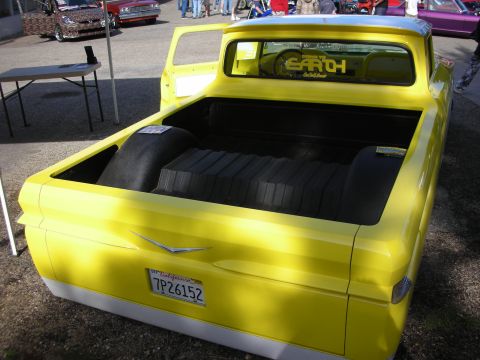 1998 Ford Crown Victoria - A bright yellow pickup truck is shown from the rear, with its bed open and customized. Other vehicles are visible in the background.