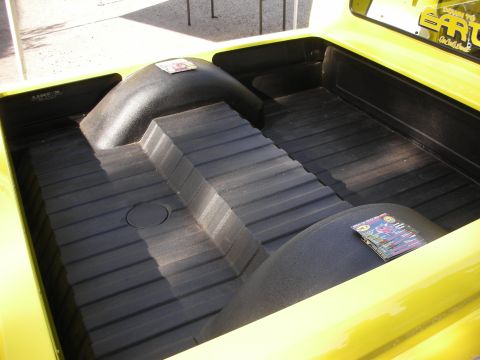 1998 Ford Crown Victoria - The black-coated interior of a yellow pickup truck bed is viewed from above, highlighting its textured surface and wheel wells.