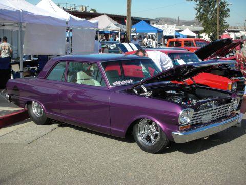 1998 Ford Crown Victoria - A custom purple 1966 Chevrolet Nova is displayed with its hood open at a car show, with other vehicles and tents in the background.