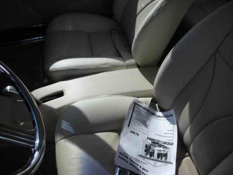 1998 Ford Crown Victoria - The interior of a car features light tan leather seats and a chrome steering wheel, with a flyer resting on the passenger seat.