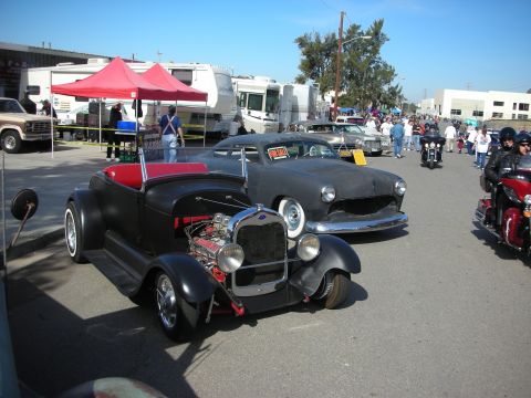 1998 Ford Crown Victoria - A black hot rod convertible is parked on the street, with other vehicles and people in the background.