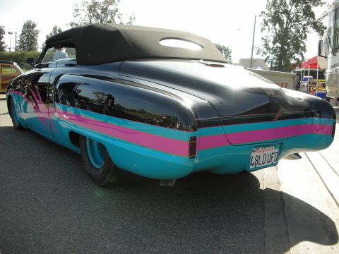 1998 Ford Crown Victoria - A customized classic convertible with a black top and vibrant side stripes is parked outdoors.