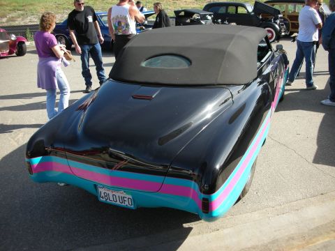 1998 Ford Crown Victoria - A customized black convertible with vibrant stripes is parked outdoors with other vehicles and people.