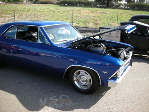 1998 Ford Crown Victoria - A blue 1966 Chevrolet Chevelle SS coupe is parked with its hood open, revealing the engine bay.