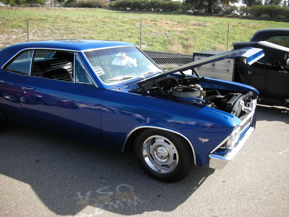 Blue 1960s muscle coupe with raised hood showing engine, beside a black car