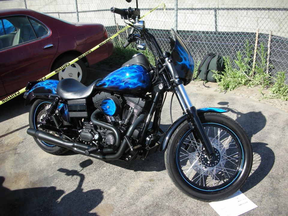Black Harley-Davidson Dyna with blue flame paint and spoked wheels by a fence