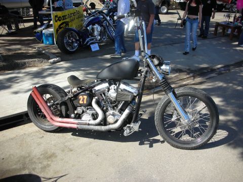 1998 Ford Crown Victoria - A custom bobber motorcycle with a black fuel tank and red exhaust pipes is parked outdoors, with another motorcycle visible in the backgrou…