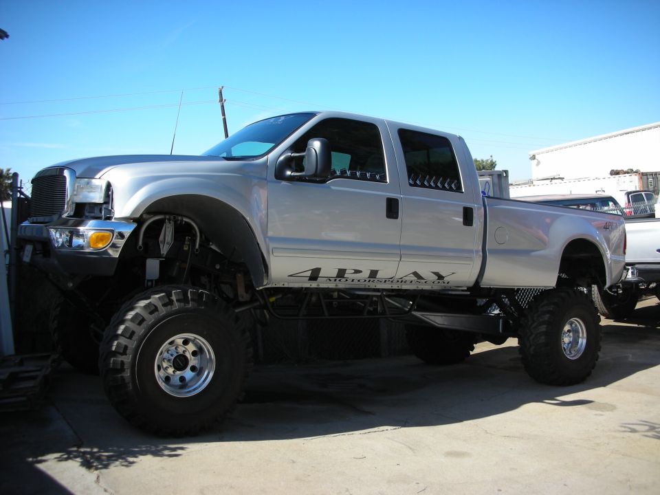 Silver lifted crew-cab pickup with 4PLAY graphics on oversized off-road tires