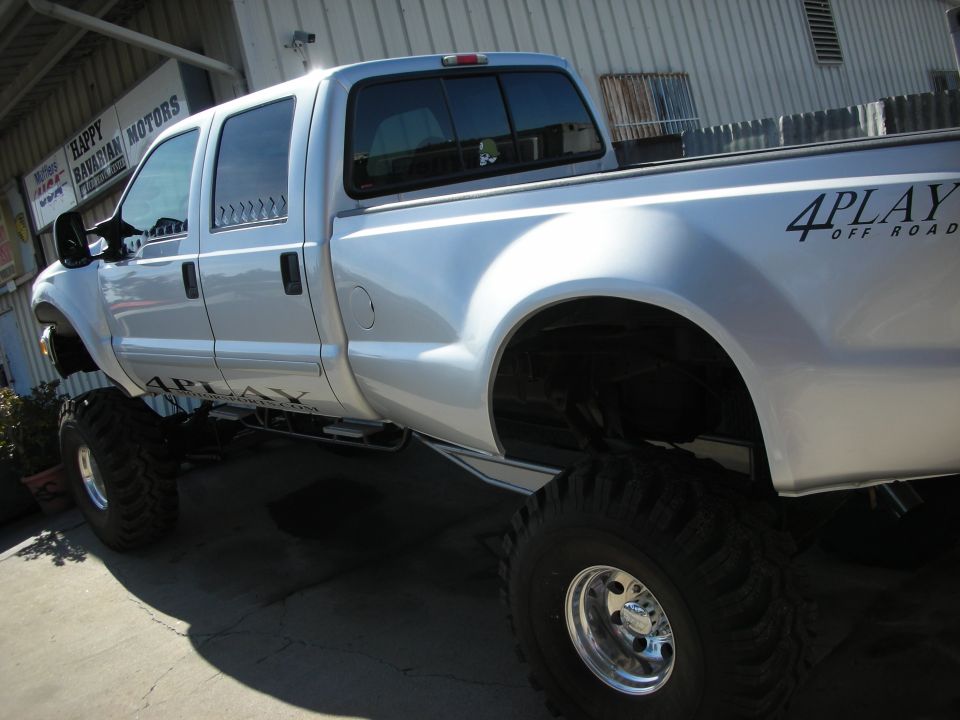 White lifted crew-cab pickup with 4PLAY Off Road graphics on huge mud tires