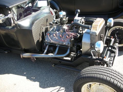 1998 Ford Crown Victoria - A close-up view of a hot rod's engine and chassis, custom exhaust and chrome details, with another vehicle visible in the background.