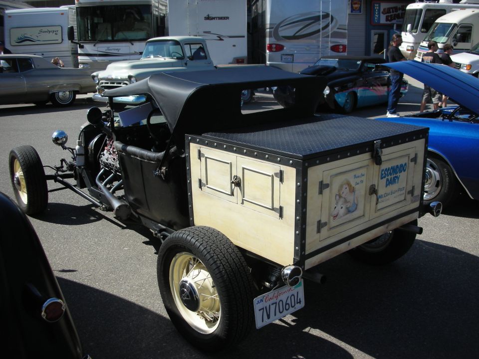 Rear three-quarter of a black T-bucket hot rod with a wood trunk box lettered Escondido Dairy