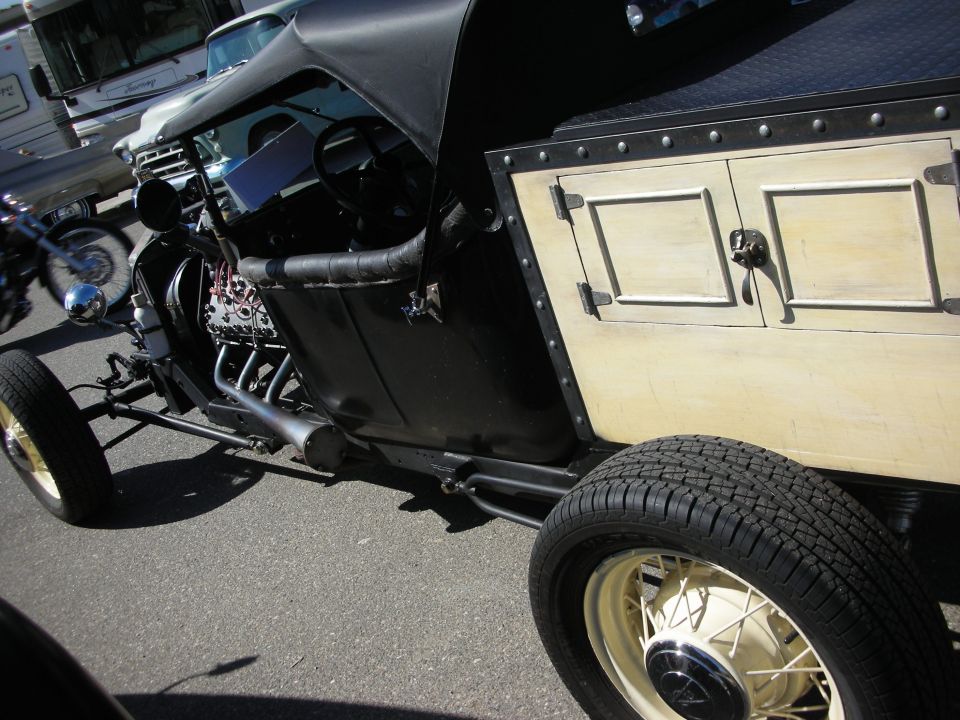 Side detail of a bare-frame hot rod showing exposed engine, steering, and a wooden cabinet body
