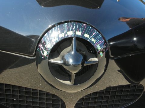1998 Ford Crown Victoria - Close-up of a black car's front emblem, a chrome star and a decorative ring with colorful paint splatters.