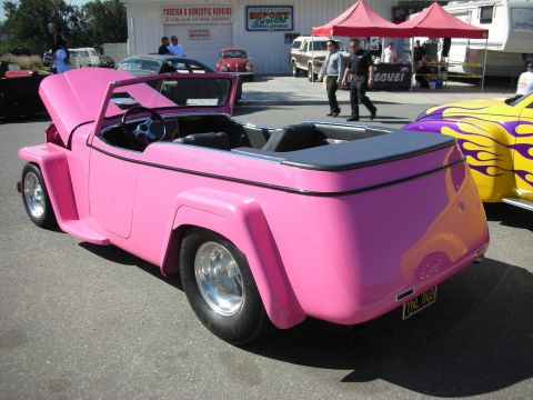 1998 Ford Crown Victoria - A bright pink convertible is parked next to a yellow car with custom flame graphics.