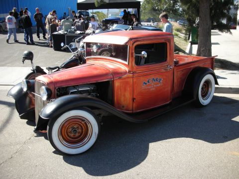 1998 Ford Crown Victoria - This vintage pickup truck, painted in a distressed orange hue, features the 'ACME Speed Shop' logo on its door and wide whitewall tires.