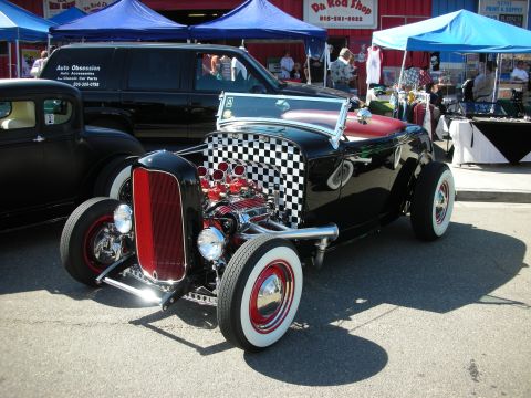 1998 Ford Crown Victoria - A custom hot rod is displayed at an outdoor event with other vehicles and vendor tents.