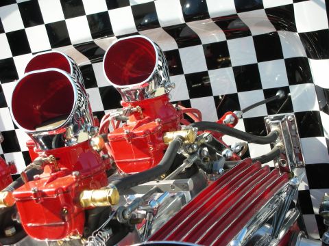 1998 Ford Crown Victoria - Close-up of a modified engine dual carburetors and chrome air intakes against a checkered flag pattern.