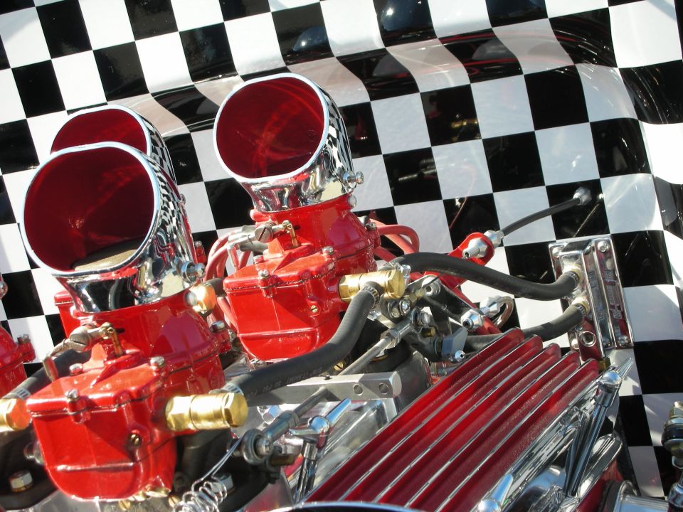 Close-up of dual red carburetors with chrome velocity stacks over a checkered backdrop