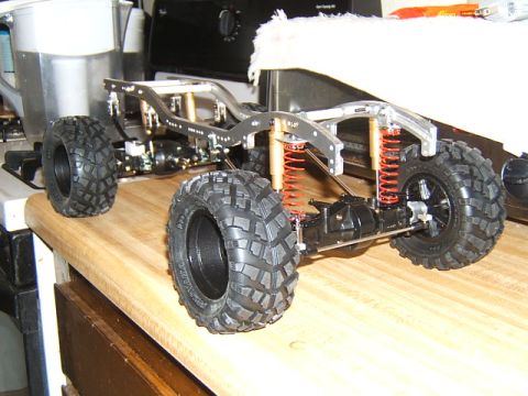 1988 Ford Bronco - The chassis of an RC crawler sits on a wooden countertop, showing its suspension and large tires.