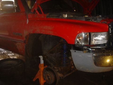 1979 Ford F-250 - A red pickup truck is undergoing repairs, with its hood open and front wheel removed, resting on jack stands.