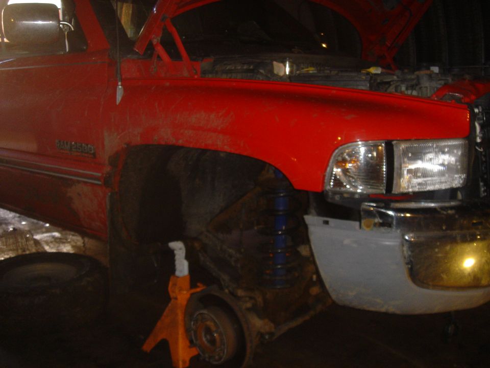 Red pickup truck on jack stands with front wheel removed and hood open