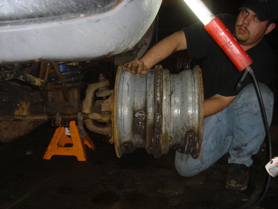 Man holding a rusty wheel hub assembly under a vehicle supported by jack stands