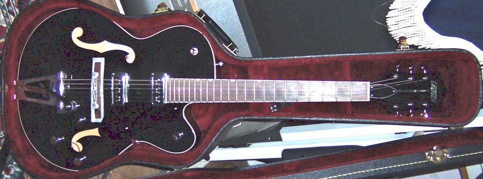 Black Gretsch hollow-body electric guitar lying in a red velvet-lined hard case