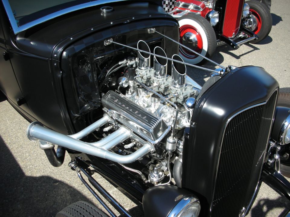 Matte-black hot rod with exposed chrome engine, triple velocity stacks, and zoomie headers