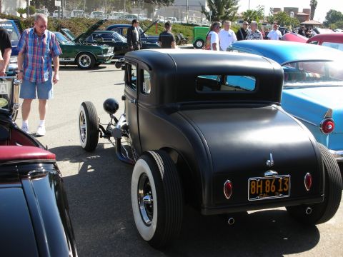 1998 Ford Crown Victoria - A black hot rod coupe is parked at an outdoor car show, with other vehicles visible in the background.
