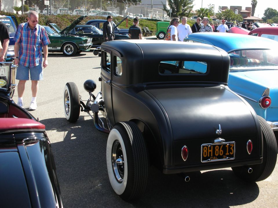 Black matte five-window hot rod coupe from rear at a car show with classic cars