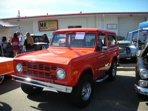 1998 Ford Crown Victoria - A bright red first-generation Ford Bronco is parked at an outdoor event, with other vehicles visible in the background.