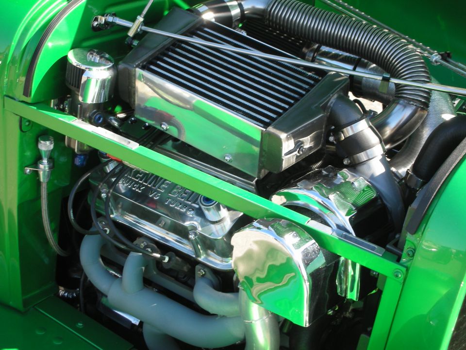Polished supercharged V8 engine in a bright green hot rod engine bay
