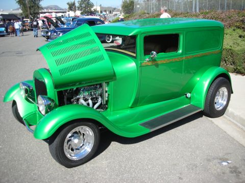 1998 Ford Crown Victoria - A bright green panel van hot rod is parked outside with its hood up, revealing the engine. Other vehicles are visible in the background.