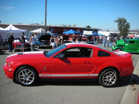 1998 Ford Crown Victoria - A red Ford Mustang GT 500 is parked at an outdoor car show with other vehicles and people.