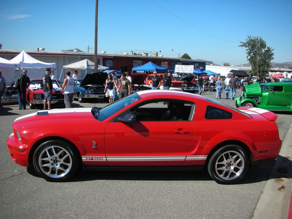 Red Shelby GT500 Mustang coupe with white racing stripes side profile at a car show