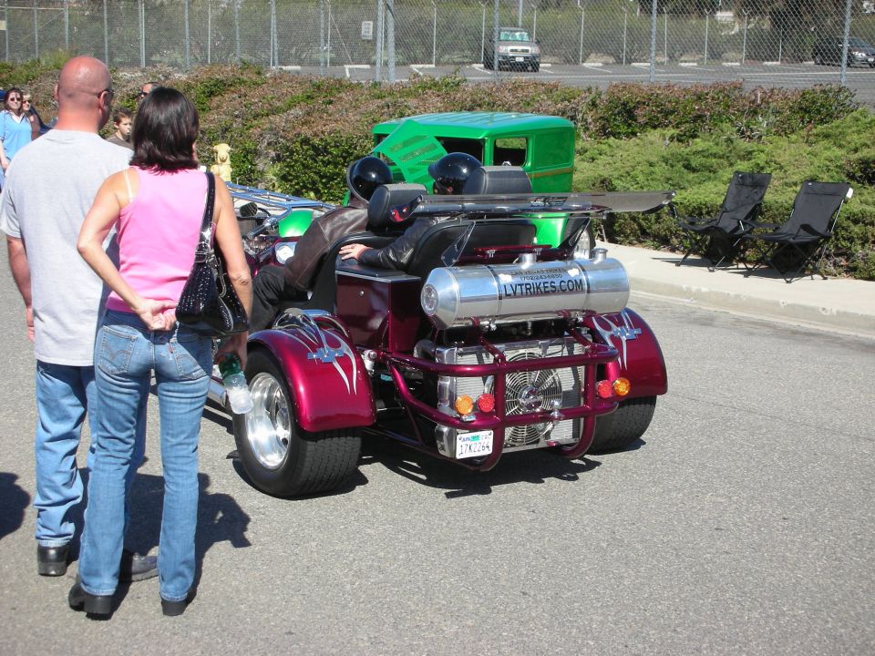 Rear of purple custom trike with chrome supercharged engine, spectators nearby