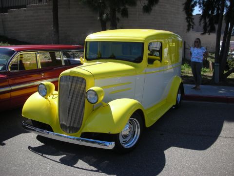 1998 Ford Crown Victoria - A two-tone yellow and white panel van is parked next to a red station wagon, with a woman standing on the sidewalk behind it.