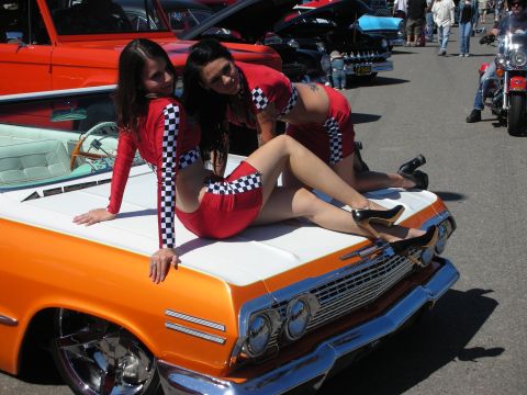 1998 Ford Crown Victoria - A car show features classic vehicles and attendees, with two women posing on the hood of a vintage car.