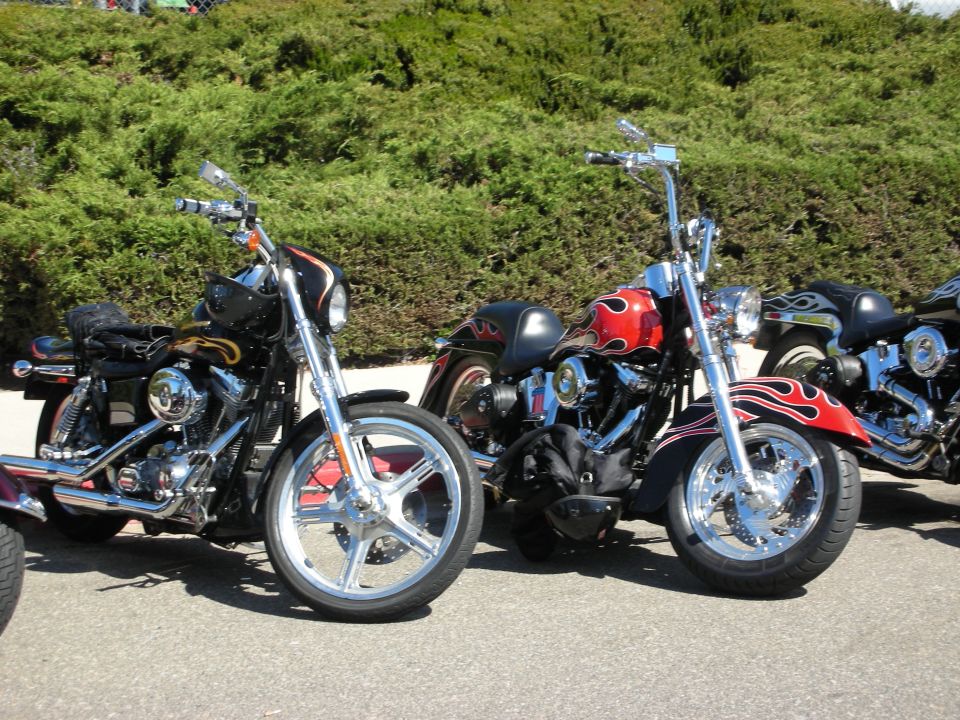 Row of custom Harley-style motorcycles, one with red flame paint, parked outdoors