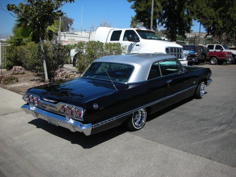 1998 Ford Crown Victoria - A classic black 1963 Chevrolet Impala with a silver roof is parked in a lot with other vehicles.