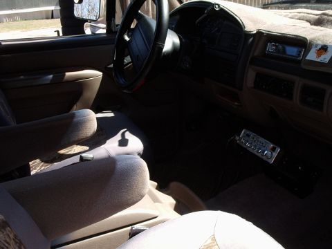 1996 Ford Bronco - Tan cloth interior of an OBS Ford truck/SUV shot from the passenger side, showing the black four-spoke steering wheel, tan dash with afterm…