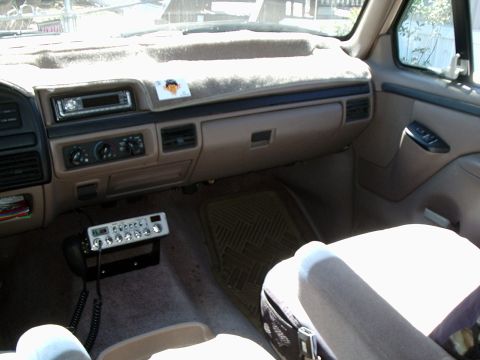 1996 Ford Bronco - Passenger side of a tan OBS Ford dash with a sheepskin-style dash cover, aftermarket single-DIN CD head unit, rotary HVAC controls and a ch…
